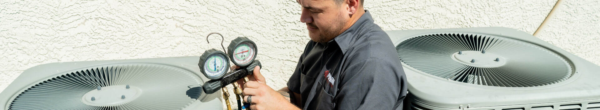 A man from Paragon Services Pros checks a thermometer beside two air conditioning units for temperature assessment.