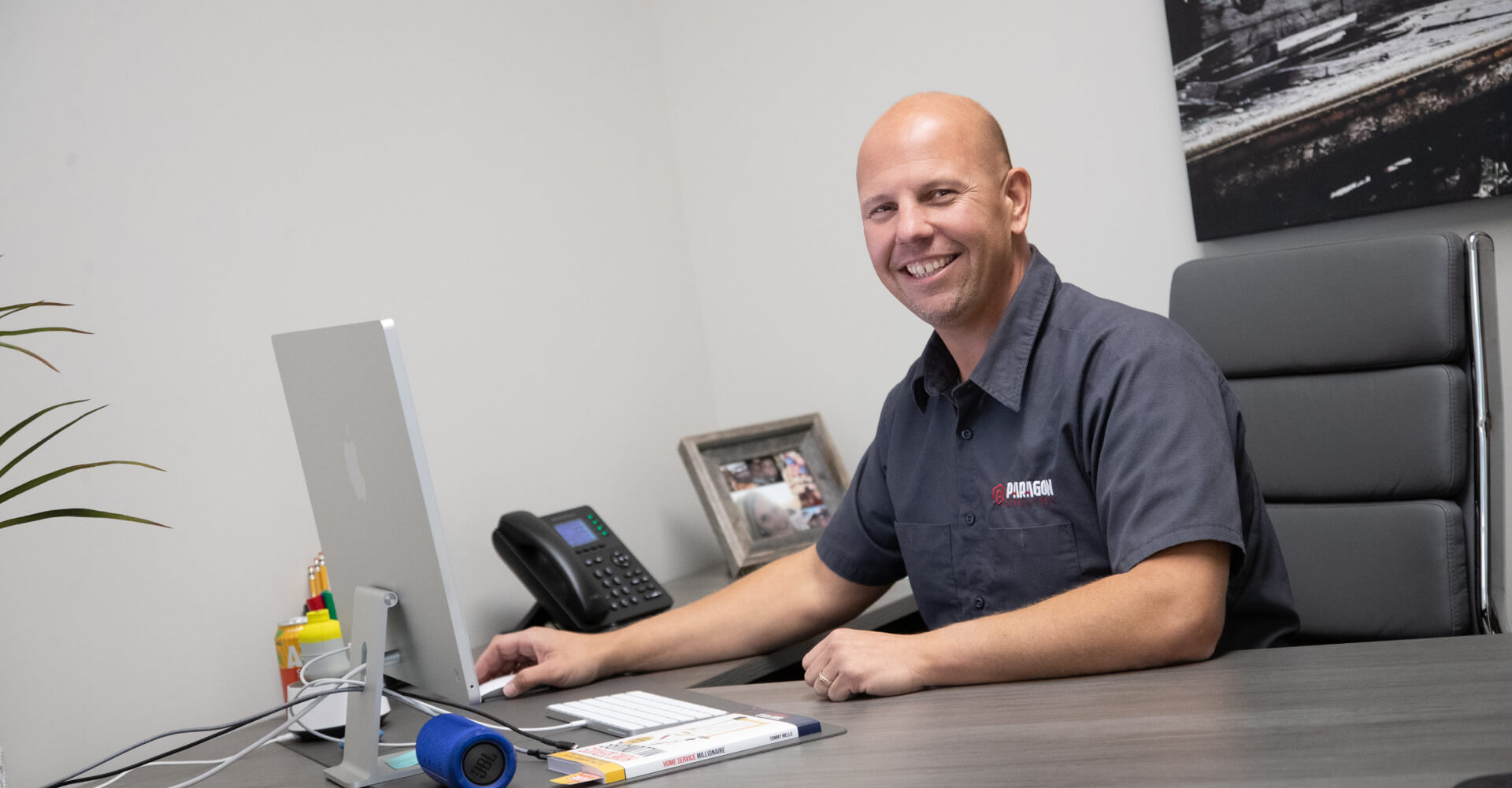 A bald man in a grey shirt seated at a desk, representing Paragon Services Pros in a professional setting.