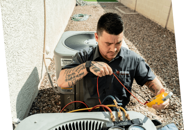 A skilled technician with tattoos from Paragon Service Pros is diligently working on an HVAC unit, demonstrating his craft.