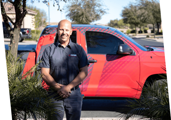 A man stands confidently in front of a red truck, representing Paragon Service Pros with professionalism and pride.
