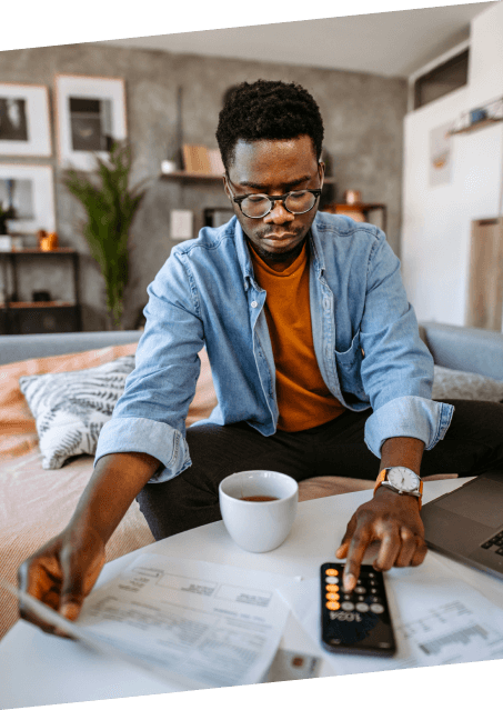 A man wearing glasses sits on a couch with a laptop, coffee cup, and calculator, focused on his work for Paragon Service Pros.