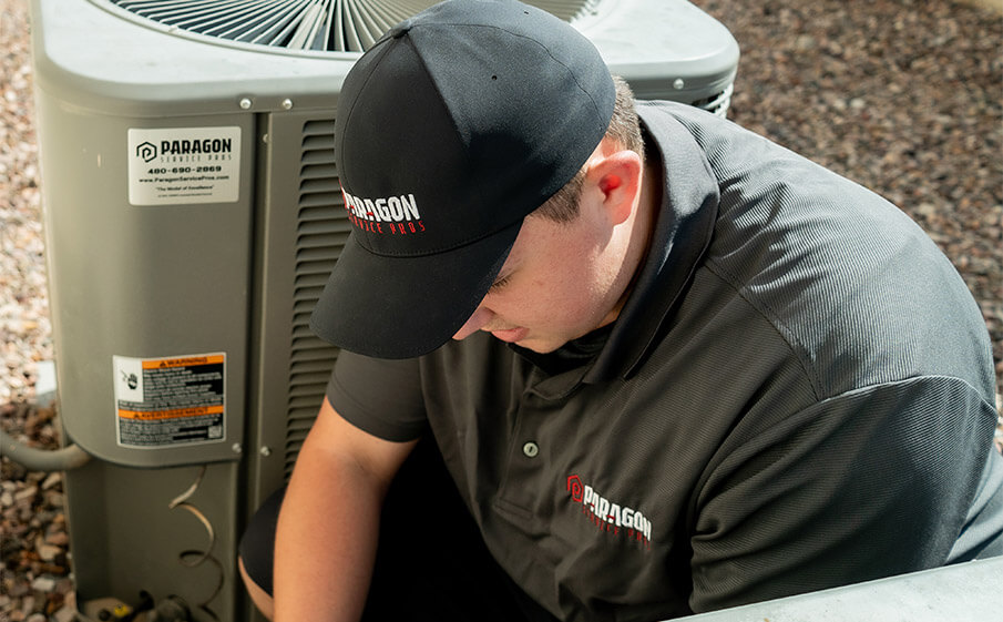 A technician in a black shirt and cap repairs an air conditioner, representing Paragon Service Pros' expertise.