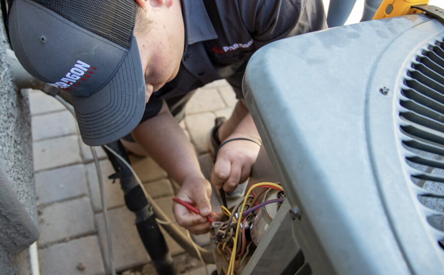 A technician from Paragon Service Pros is diligently repairing an air conditioner in a residential setting