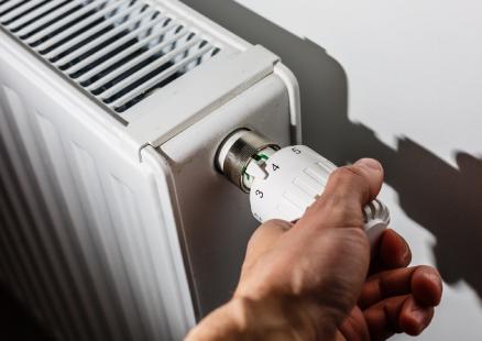 A person adjusts a thermostat on a radiator, showcasing Paragon Service Pros' expertise in home heating solutions.