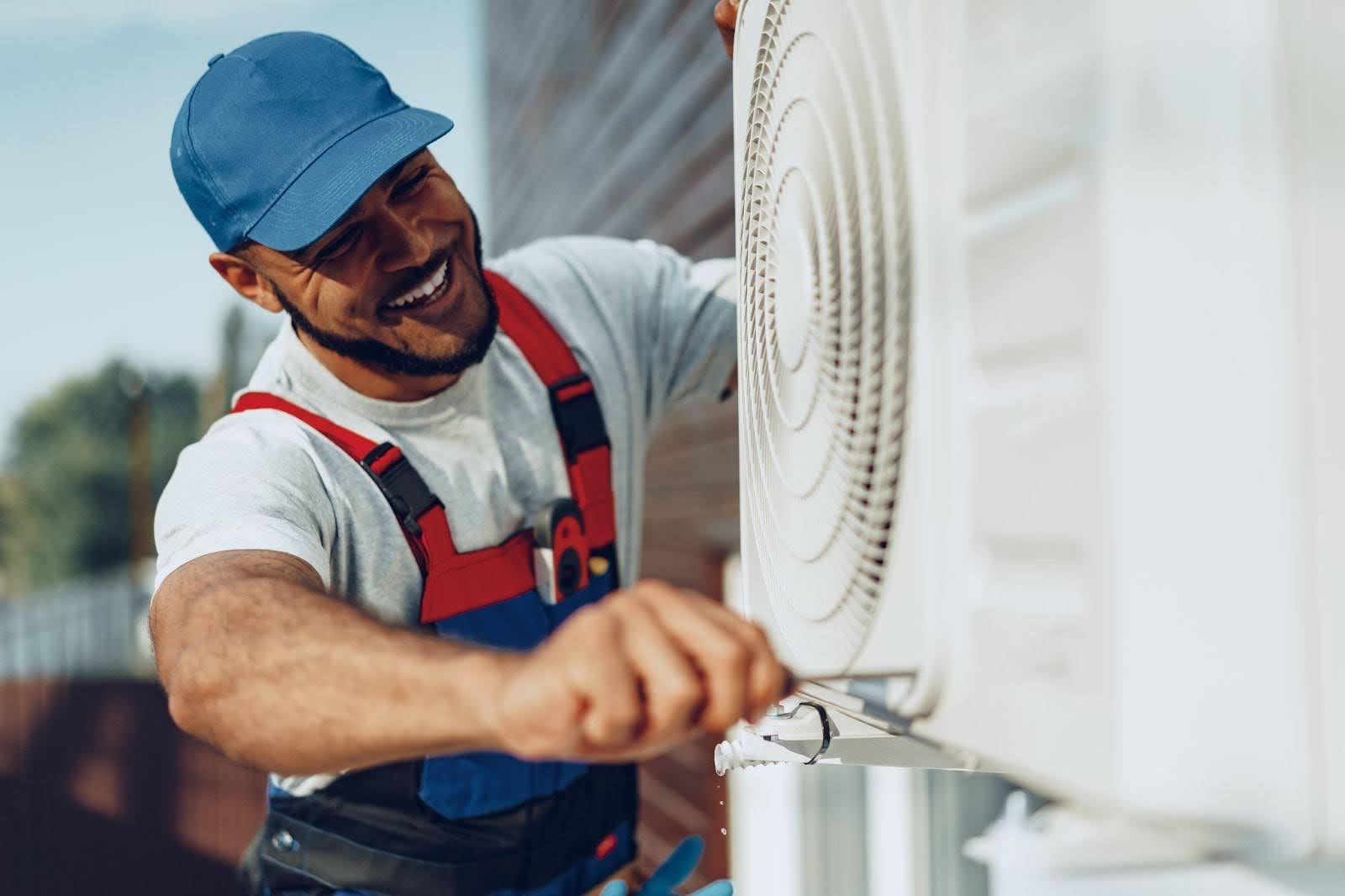 A man in overalls and a hat repairs an air conditioner in a home setting