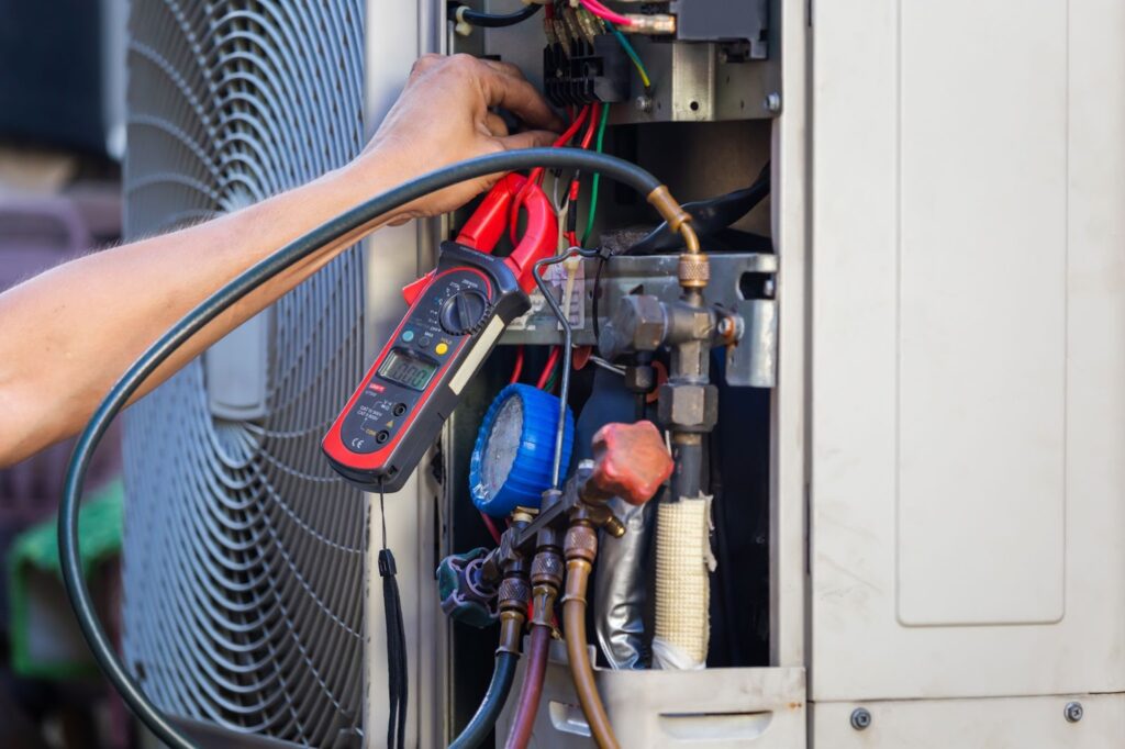 Hand using a clamp meter to test an air conditioning unit's internal components.