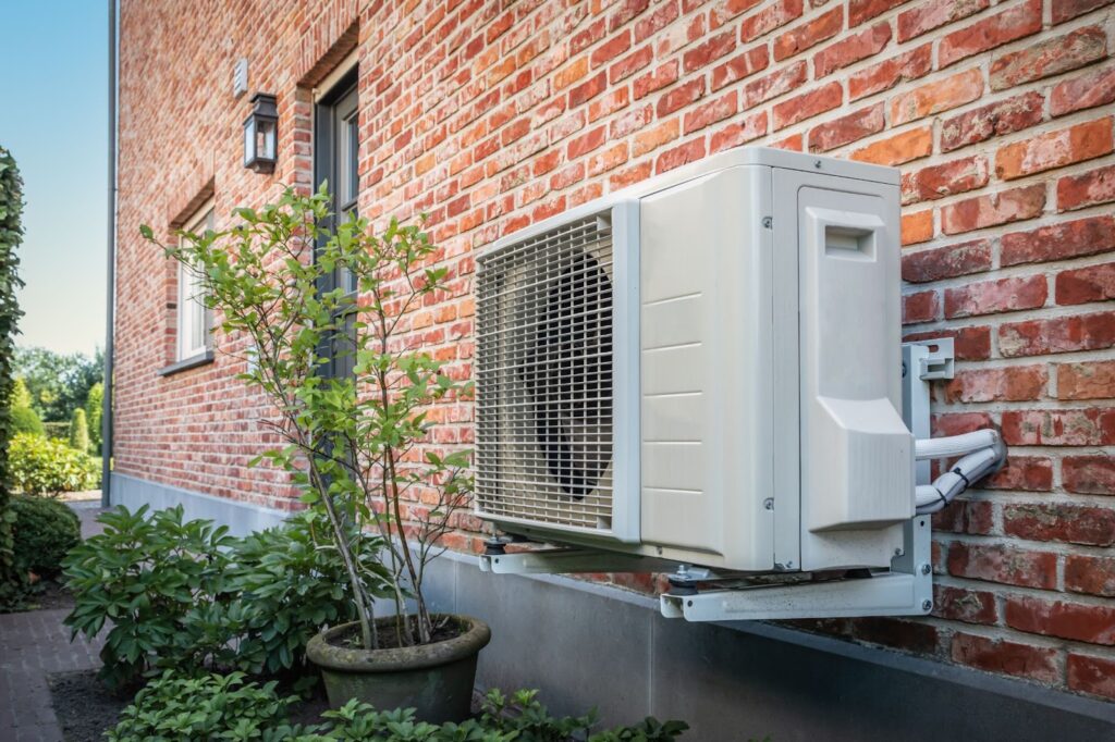 Outdoor air conditioning unit mounted on a brick wall with greenery nearby.