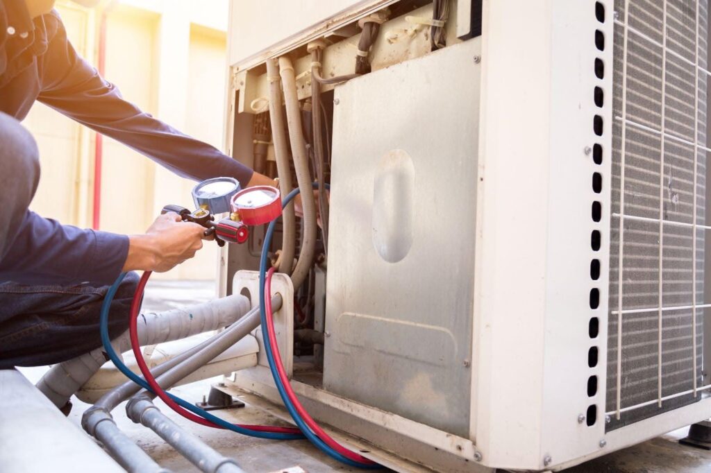 A man repairs an air conditioner focused on the unit with tools in hand in a well-lit indoor setting