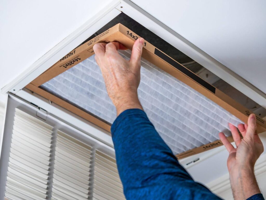 A man installs a filter on a ceiling fan focusing on the task with tools in hand and a ladder nearby