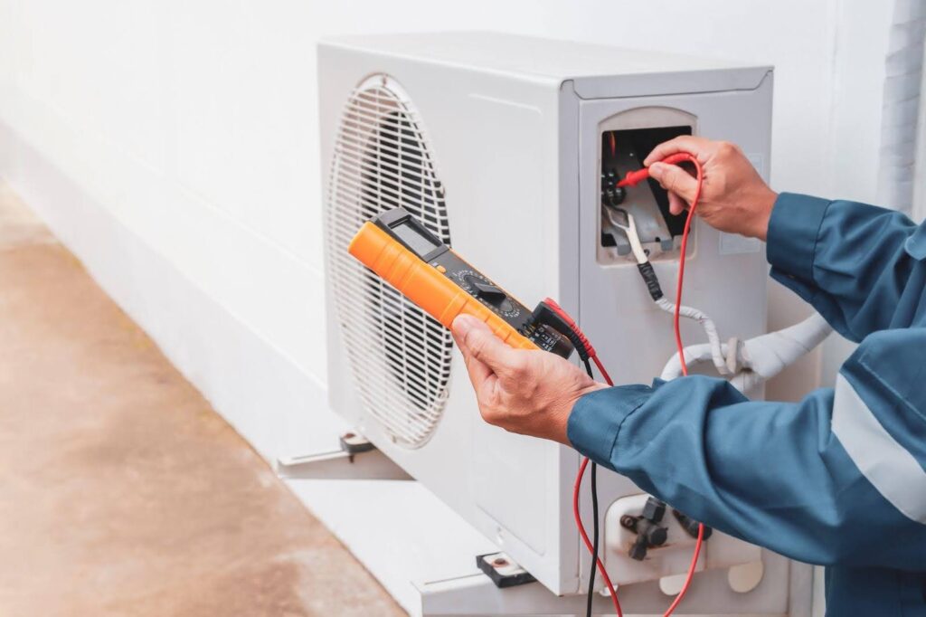 A man repairs an air conditioner focused on the unit with tools in hand in a well-lit indoor setting
