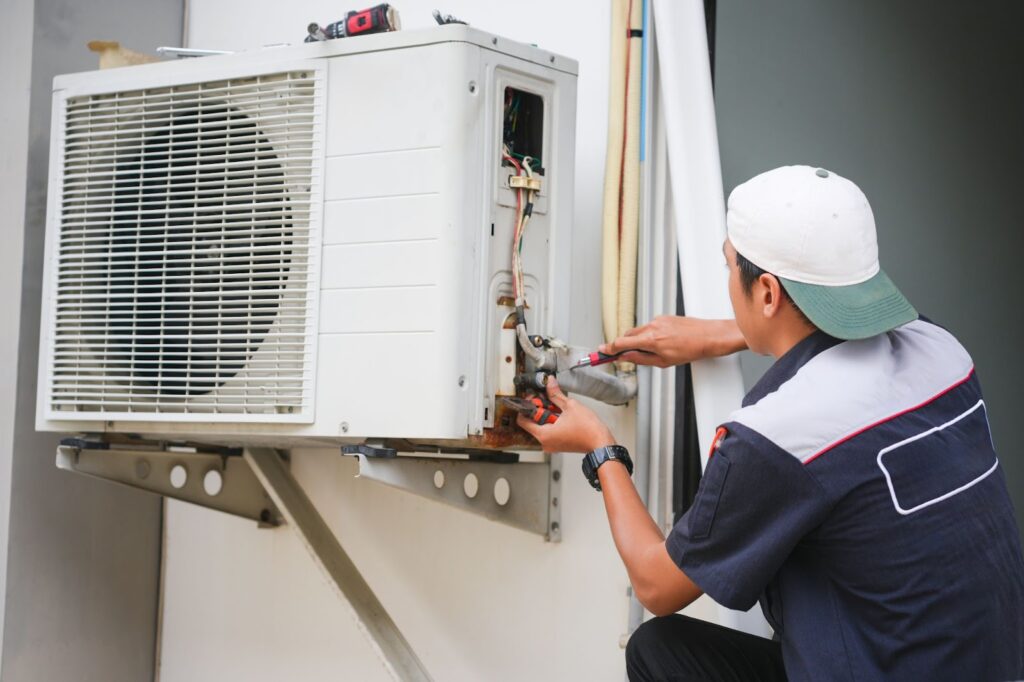 A technician servicing an outdoor air conditioning unit using hand tools.